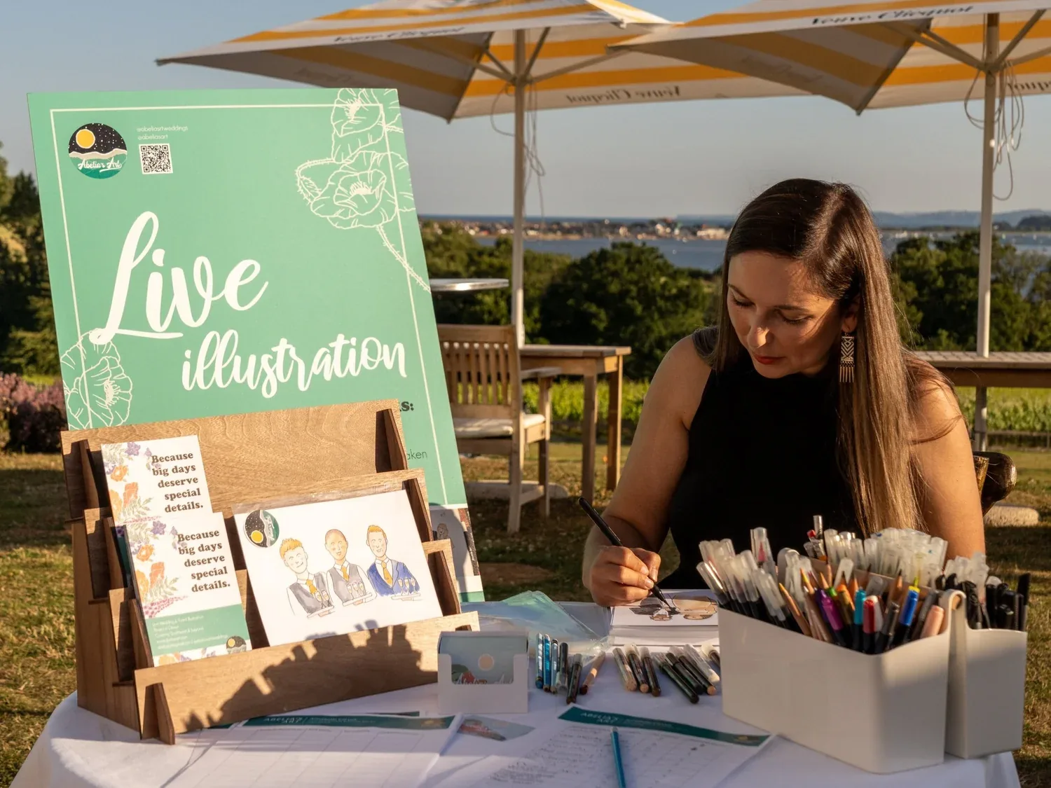 Annabelle drawing at her table outdoors at Lympstone Manor, with the estuary behind