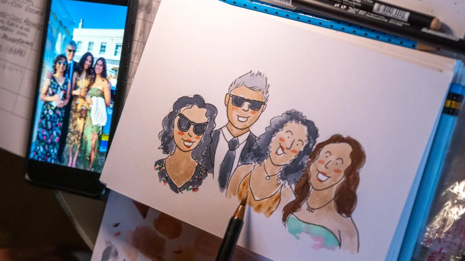 Work in progress: a group of guests taking shape in watercolour, phone photo propped as reference
