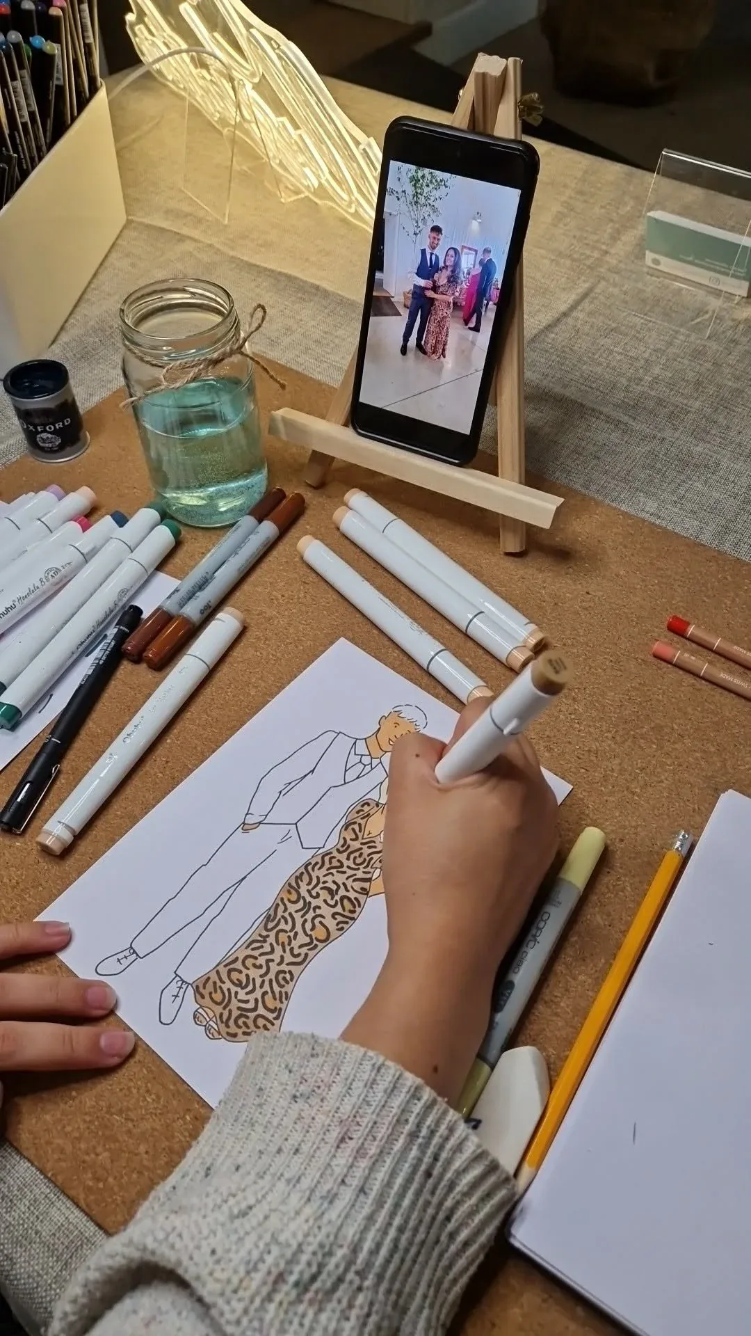 A couple's portrait taking shape on paper, drawn from a photo propped on a little easel
