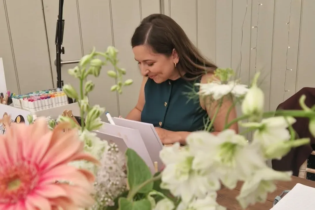 Annabelle sketching wedding guests behind a vase of blush and white flowers