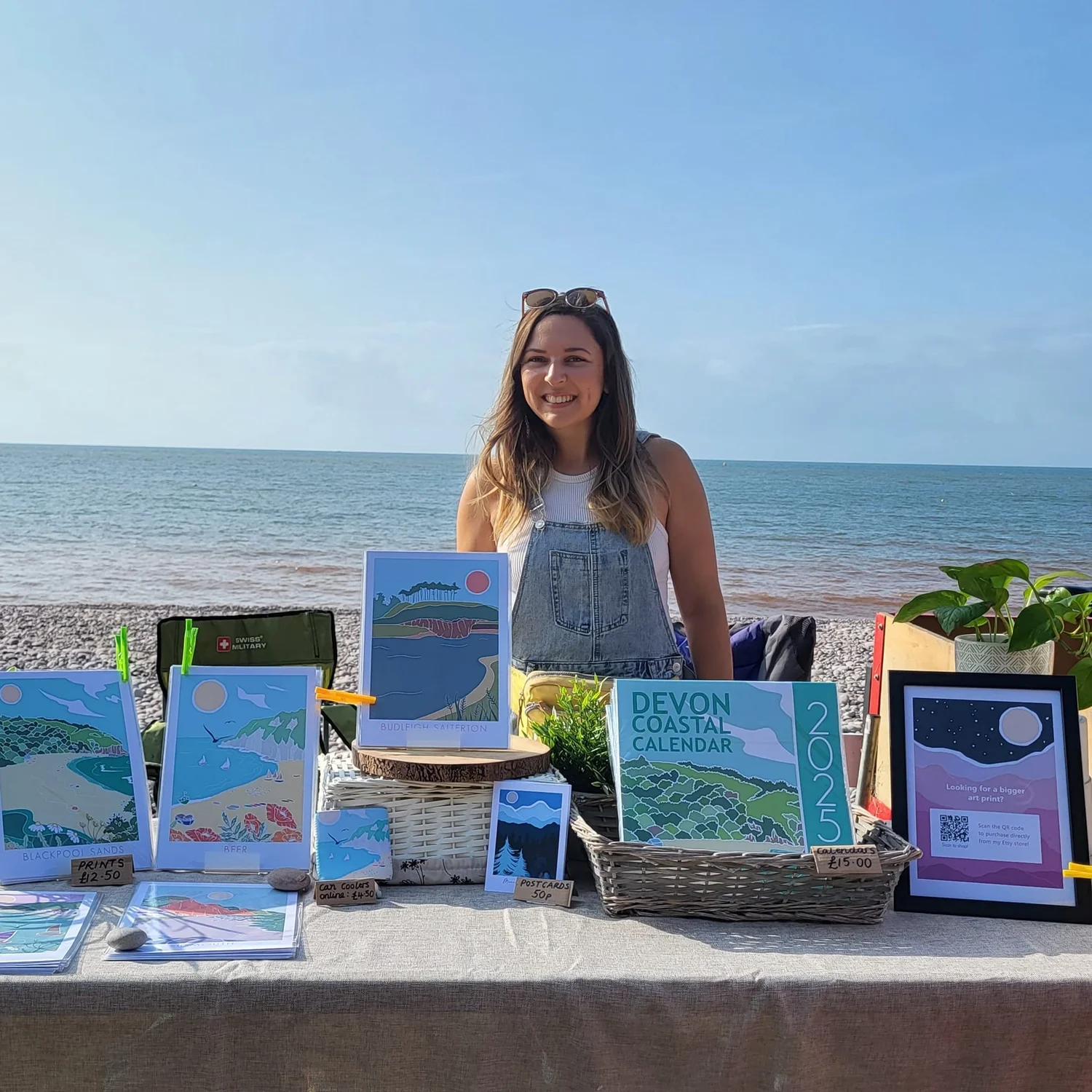 Annabelle at her print stall on a Devon beach, sea behind her